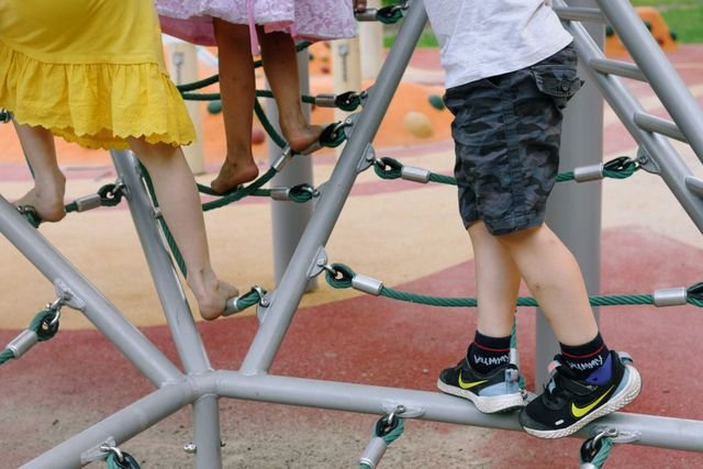 Children playing and climbing on playground ropes on a sunny summer day.